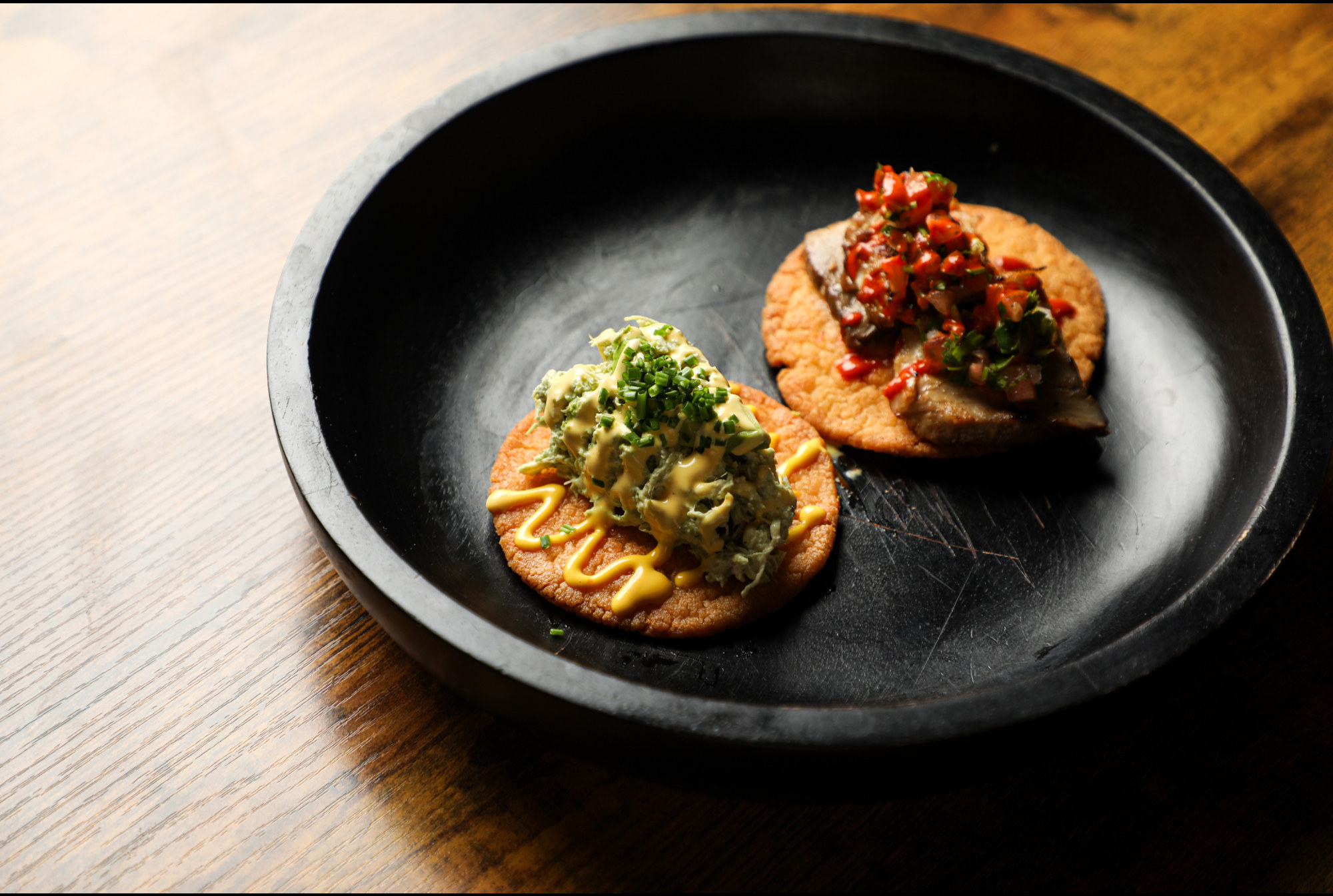 Two carefully plated savory bites on a black plate